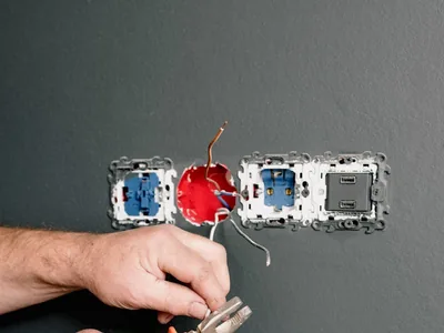 Electrician using pliers to repair wiring at electrical outlets in a residential wall